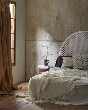 Cabecero Nordal de ratán blanco junto a una ventana con cortinas y ropa de cama clara