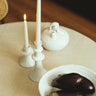 Candelabro bajo de gres blanco con relieves de Leandro Cano: candelabro bajo y alto con velas encendidas, botijo y frutero sobre mesa.