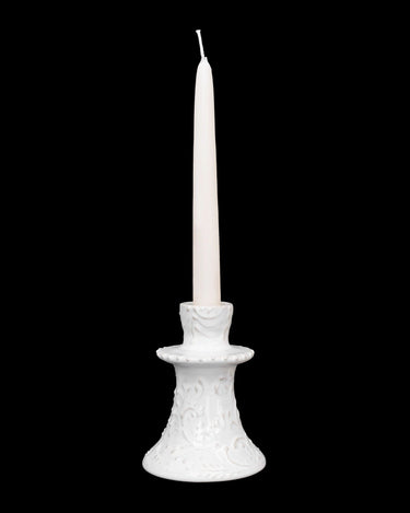 Candelabro de Leandro Cano: candelabro bajo blanco con vela larga sobre fondo negro.