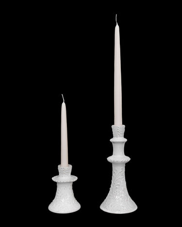 Pareja de candelabros de alturas distintas con velas blancas.