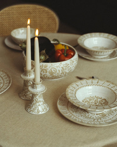 Candelabro Leandro Cano con vela encendida en una mesa de vajilla blanca y beige y verduras