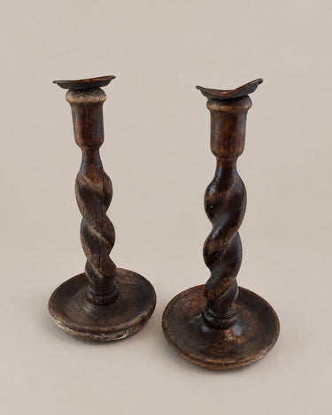 Candeleros antiguos de madera torneada oscura en pareja, vista frontal con ambas bases completas