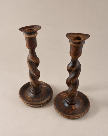 Candeleros de madera torneada oscura vistos completos en perspectiva, con luces y sombras suaves