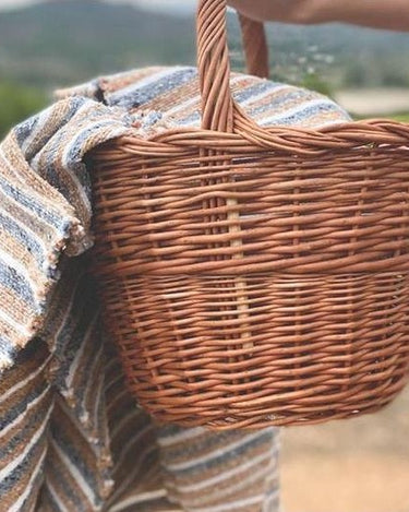 Cesta ovalada de mimbre con asa reforzada de Cestería Aparici, con una tela, en un entorno exterior