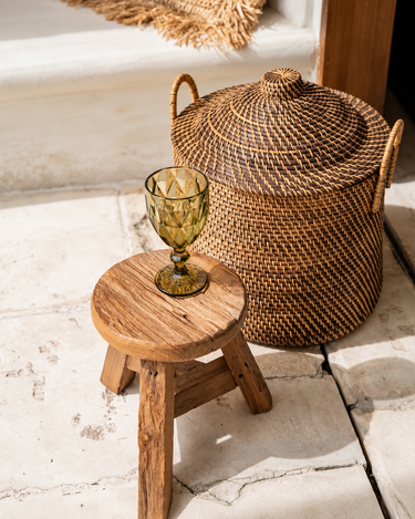 Cesta de ratán con tapa y asas, junto a un taburete con una copa