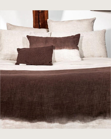 Cojín marrón de algodón con degradado artesanal, cojines marrones y blancos sobre una cama
