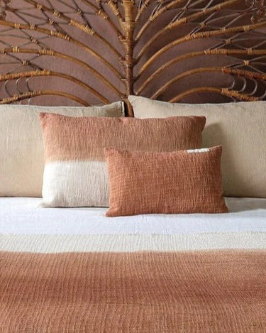 Cojín pequeño de algodón color galleta de Bed and Philosophy, sobre una cama con cabecero de fibras
