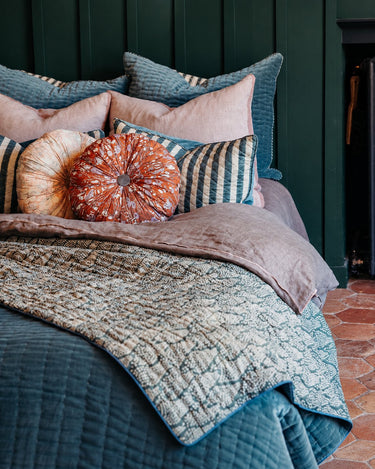 Composición de cama con el cojín rosa floral junto a un cojín circular naranja