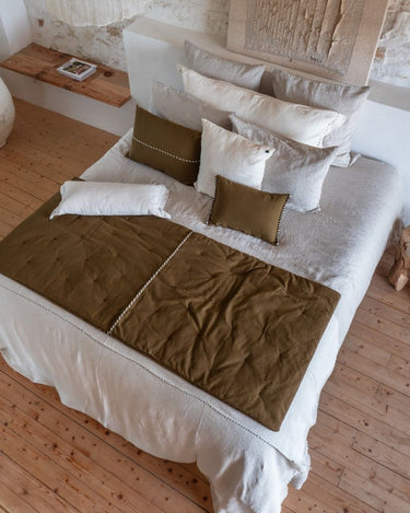 Colcha boutis de algodón y lino color bronce de Bed and Philosophy, sobre una cama blanca con cojines coordinados