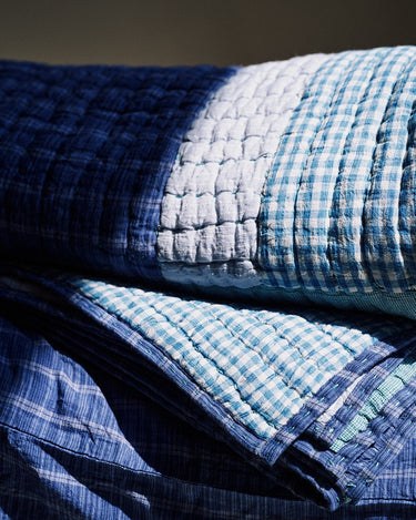 Detalle de cuadros azules y blancos de distintas escalas y puntadas del acolchado de una colcha