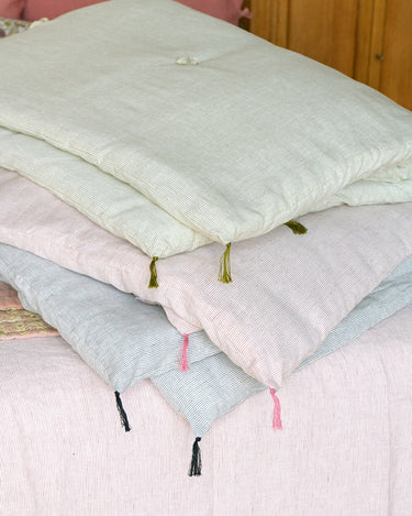 Colcha Caravane rosa doblada junto a versiones verde y gris sobre una cama