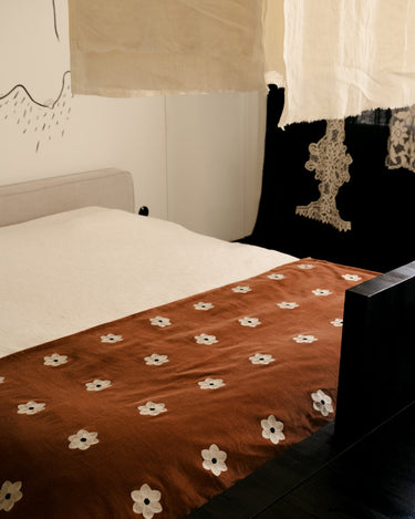 Colchoneta Daisy óxido extendida sobre una cama con textiles neutros de Olsson & Jensen