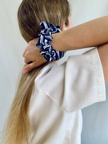 Uno de los coleteros de House of Scrunchies, azul marino y blanco, llevado en la muñeca junto al cabello