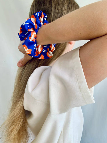 Uno de los coleteros de House of Scrunchies, azul y naranja, llevado en la muñeca junto al cabello