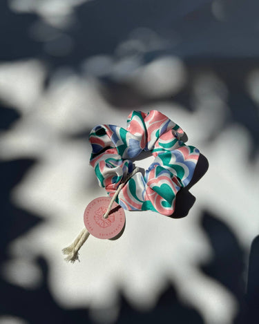 Coletero de House of Scrunchies: coletero junto a sombras de plantas, modelo de satén reciclado azul, rosa y verde