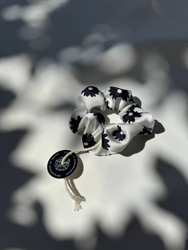 Coletero de House of Scrunchies: coletero junto a sombras de plantas, modelo de satén reciclado con flores negras