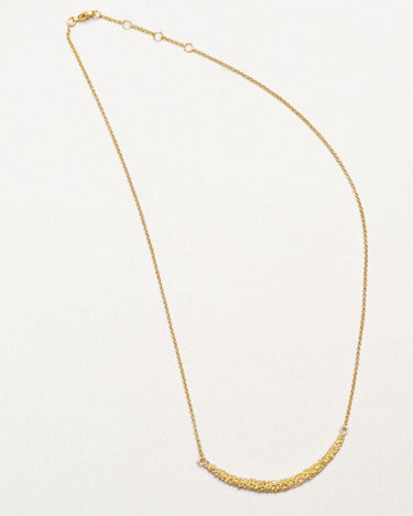 Un collar dorado de bolitas extendido sobre superficie clara; cadena, mosquetón y extensión visibles.