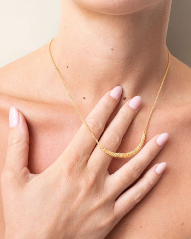 Collar de Joidart: detalle de collar dorado de bolitas puesto al cuello, mano sosteniendo suavemente el motivo central.