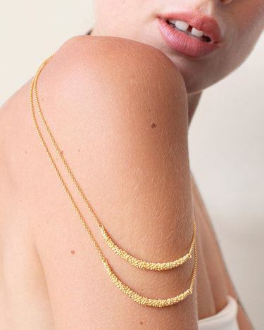 Dos collares dorados de bolitas colocados sobre el hombro de una modelo.