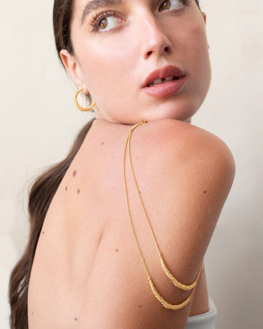 Modelo con dos collares dorados sobre el hombro y pendientes adicionales de atrezzo.