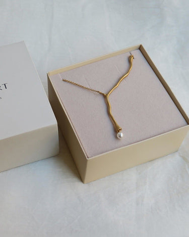 Collar dorado sinuoso con extremo blanco colocado en caja clara.