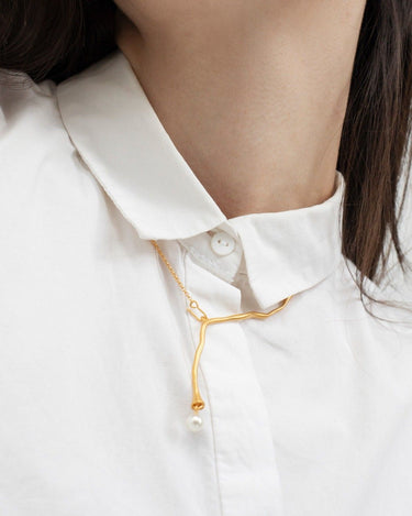 Collar de Joidart: collar dorado sinuoso con extremo blanco, llevado sobre camisa blanca abotonada.