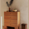 Cómoda alta de chapa de roble con cuatro cajones de Ferm Living: cajonera alta de cuatro cajones superpuestos, con jarrón y frutero junto a pared clara.