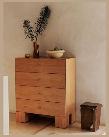 Cómoda alta de chapa de roble con cuatro cajones de Ferm Living: cajonera alta de cuatro cajones superpuestos, con jarrón y frutero junto a pared clara.