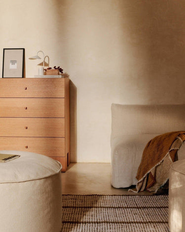 Cómoda de Ferm Living: cajonera junto a asiento claro con manta; cuadro y lámpara sobre el mueble.