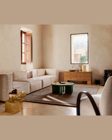 Una de las cómodas bajas Kuben al fondo del salón, con sofá claro y mesa verde en primer plano.