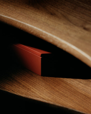 Detalle de una de las consolas de Ferm Living, con una caja roja entre las dos superficies de nogal.