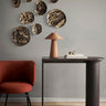 Consola de roble oscuro con apoyo cilíndrico de Ferm Living, roble oscuro: consola oscura bajo platos de pared y lámpara de ratán.