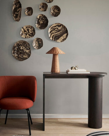 Consola de roble oscuro con apoyo cilíndrico de Ferm Living, roble oscuro: consola oscura bajo platos de pared y lámpara de ratán.