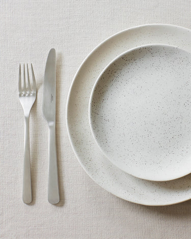 Cubiertos de acero cepillado junto a un plato de gres