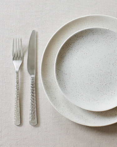 Cubiertos martillados junto a un plato de gres claro