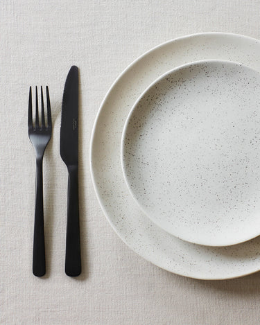 Cubiertos negros mate junto a un plato claro