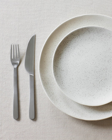 Cubiertos satinados mate junto a un plato de gres