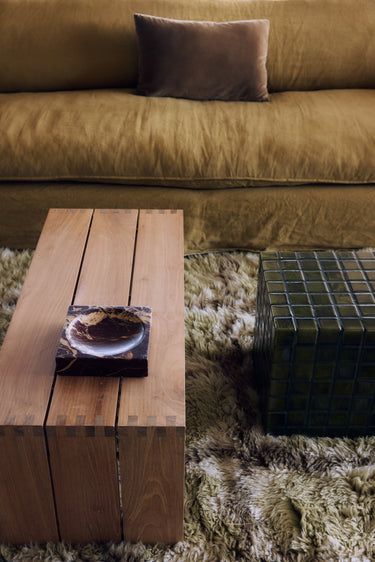 Cubo decorativo de mármol burdeos sobre una mesa baja de listones junto al sofá