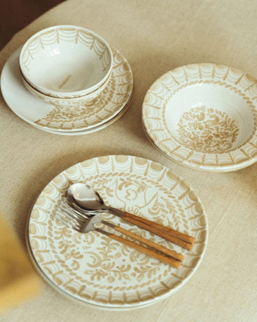 Cuencos de gres blancos y beige sobre platos en una mesa con cubiertos de mango de madera