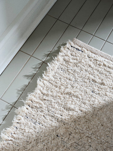 Detalle de la alfombra blanco roto extendida sobre el suelo