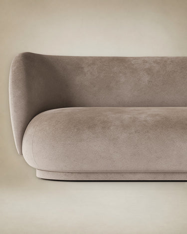 Diván de Ferm Living: detalle del brazo izquierdo, curva del respaldo y asiento del diván beige; reflejos suaves del terciopelo.