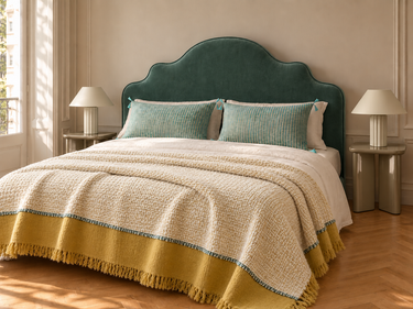 Dormitorio con cabecero de terciopelo verde agua, mesitas Garance caqui, lámparas Lizette, cojines Florio Lac y plaid Haika mostaza. Ambiente generado con IA.