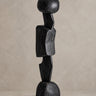 Escultura Vical de madera de teca negra sobre pared y suelo topo claro texturizado