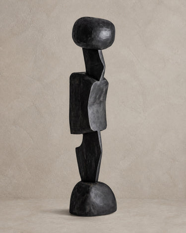 Escultura Vical de madera de teca negra sobre pared y suelo topo claro texturizado