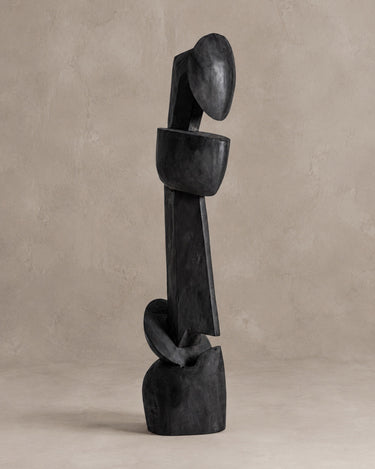 Escultura Vical de teca negro mate sobre pared y suelo topo claro texturizado