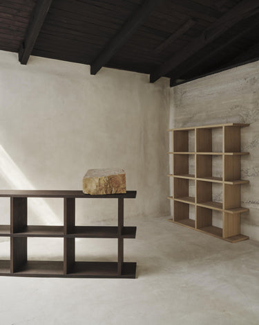 Estantería baja de chapa de roble de Ferm Living, roble oscuro: estantería baja oscura con una estantería alta clara al fondo.