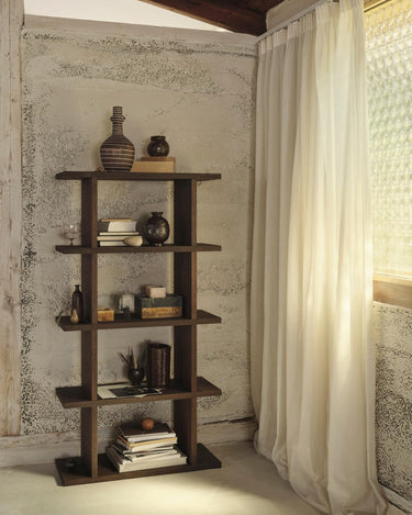 Estantería de chapa de roble de una columna de Ferm Living, roble oscuro: estantería oscura con libros y jarrones junto a una cortina clara.