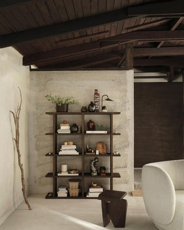 Estantería de chapa de roble de dos columnas de Ferm Living, roble oscuro: estantería oscura con libros, jarrones y lámpara junto a una silla clara.
