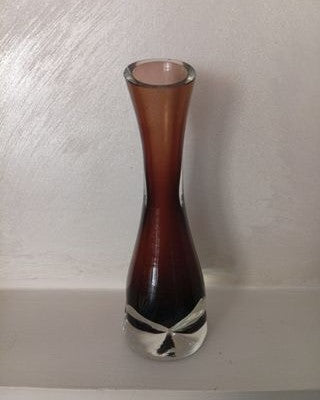 Florero vintage de vidrio marrón con base transparente y cuello estrecho, junto a una pared clara