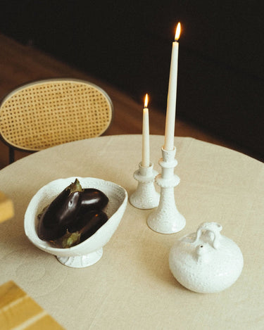 Frutero ovalado de gres blanco con pie de Leandro Cano: frutero con berenjenas junto a botijo y dos candelabros con velas encendidas.